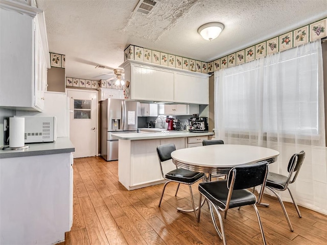 kitchen with kitchen peninsula, stainless steel fridge, ceiling fan, white cabinets, and light hardwood / wood-style floors