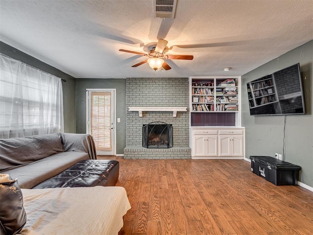 living room featuring built in shelves, light hardwood / wood-style flooring, a textured ceiling, and a brick fireplace