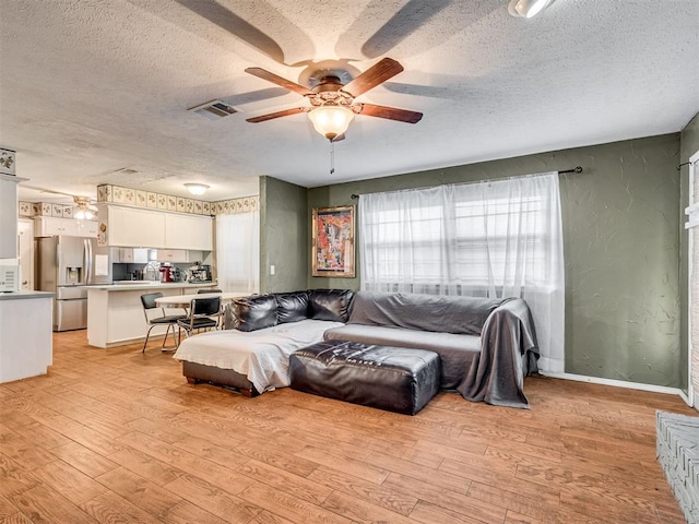 living room with ceiling fan, light hardwood / wood-style flooring, and a textured ceiling