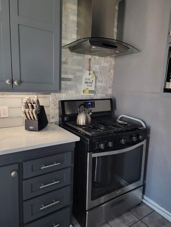 kitchen featuring light stone counters, gray cabinetry, exhaust hood, light tile patterned floors, and stainless steel range with gas cooktop