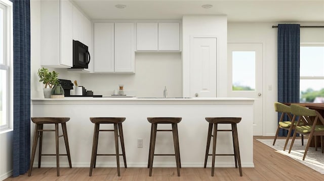 kitchen with black appliances, white cabinetry, a breakfast bar area, and light hardwood / wood-style flooring