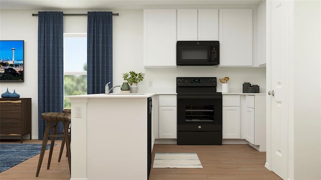 kitchen featuring kitchen peninsula, light wood-type flooring, a breakfast bar, black appliances, and white cabinetry