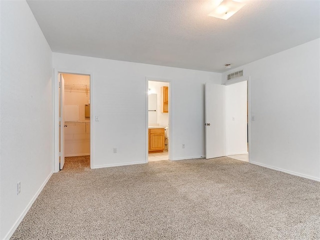 unfurnished bedroom featuring a spacious closet, a closet, ensuite bathroom, and light carpet