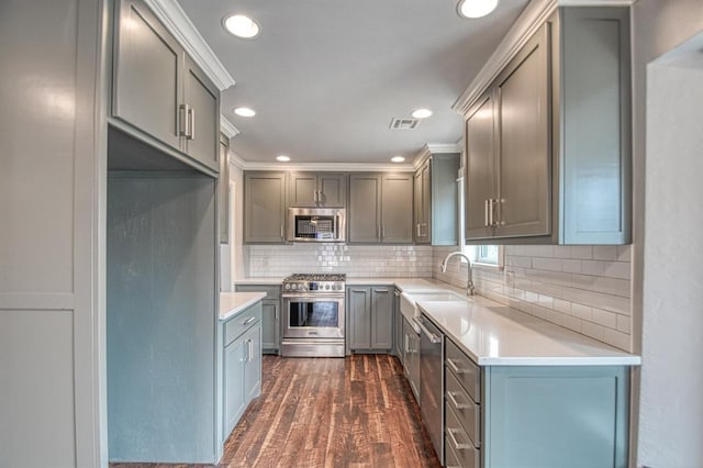 kitchen with dark wood-style floors, stainless steel appliances, light countertops, backsplash, and a sink