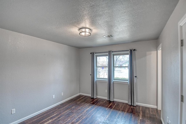 empty room featuring dark wood-style floors, visible vents, baseboards, and a textured wall