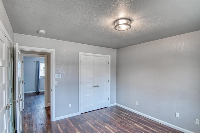 unfurnished bedroom with dark wood-type flooring, a closet, a textured ceiling, and baseboards