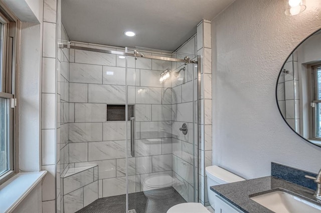 full bathroom with toilet, a textured wall, a shower stall, and vanity