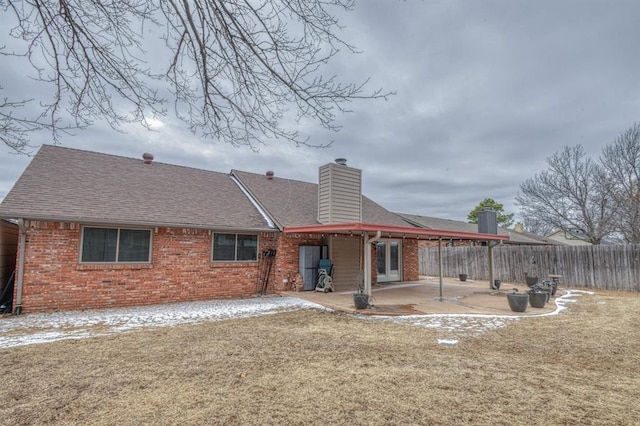 rear view of house with brick siding, fence, a yard, a chimney, and a patio area