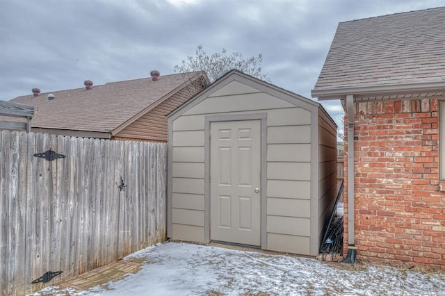 snow covered structure featuring fence, a storage unit, and an outdoor structure