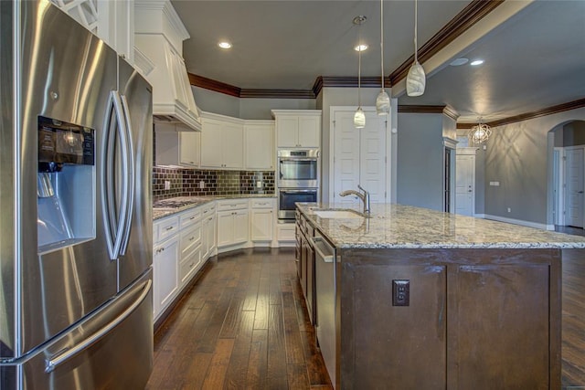 kitchen featuring pendant lighting, dark wood-type flooring, a center island with sink, sink, and appliances with stainless steel finishes