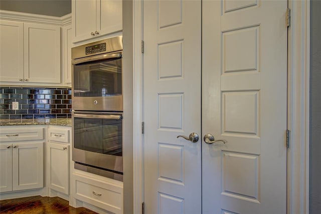 kitchen with decorative backsplash, stainless steel double oven, light stone countertops, dark hardwood / wood-style flooring, and white cabinetry