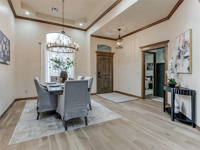 dining space with crown molding, a notable chandelier, a tray ceiling, and light wood-type flooring