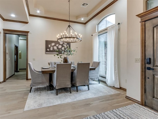 dining area featuring crown molding, a notable chandelier, light hardwood / wood-style floors, and a tray ceiling