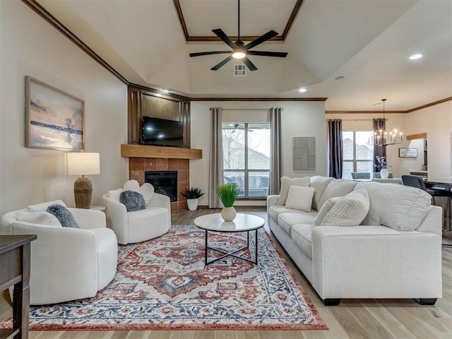 living room featuring a tiled fireplace, ornamental molding, ceiling fan with notable chandelier, and light hardwood / wood-style floors