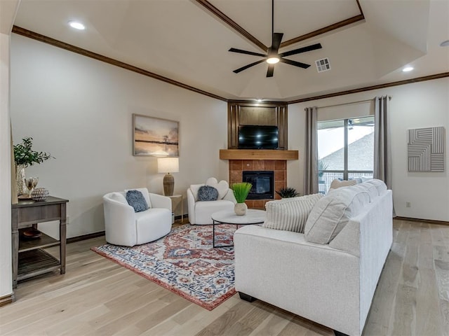 living room featuring ornamental molding, a tray ceiling, ceiling fan, a tiled fireplace, and light hardwood / wood-style floors