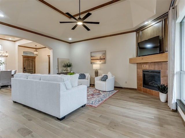 living room featuring crown molding, light hardwood / wood-style flooring, a tile fireplace, and ceiling fan