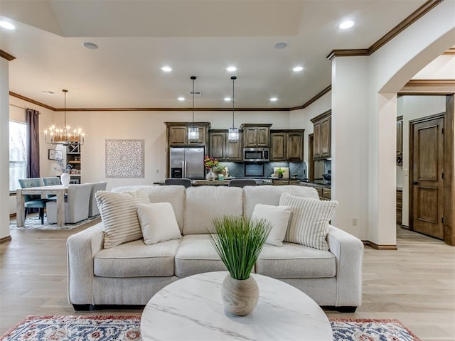 living room featuring an inviting chandelier, ornamental molding, and light wood-type flooring