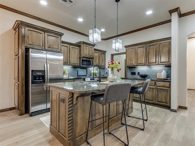 kitchen with appliances with stainless steel finishes, a kitchen island with sink, dark stone counters, and light wood-type flooring