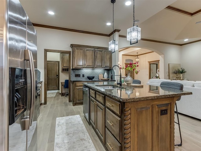 kitchen with pendant lighting, sink, appliances with stainless steel finishes, dark stone countertops, and a center island with sink