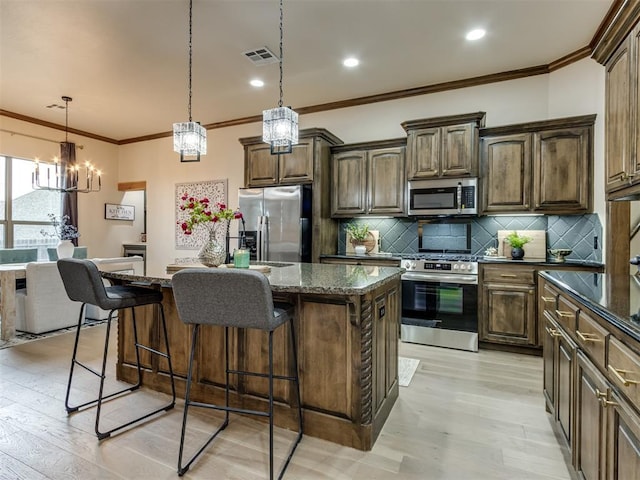 kitchen with stainless steel appliances, decorative light fixtures, a kitchen island with sink, and dark stone counters