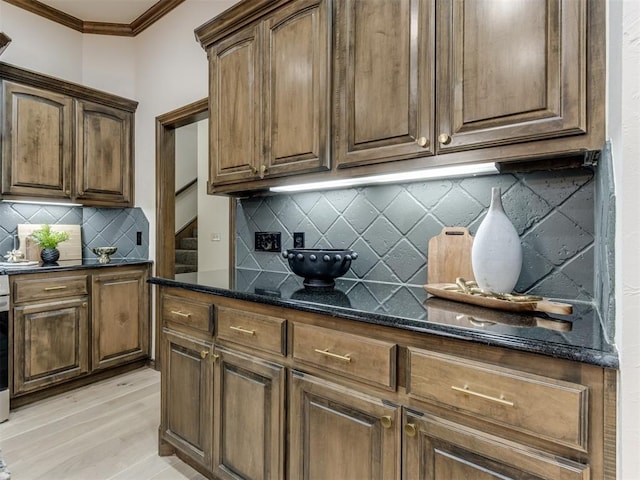 kitchen with dark stone countertops, crown molding, tasteful backsplash, and light hardwood / wood-style floors