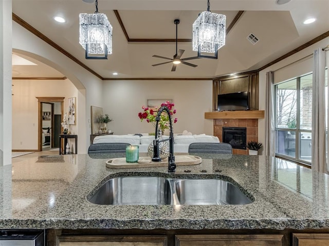 kitchen featuring light stone counters, ornamental molding, sink, and a tile fireplace