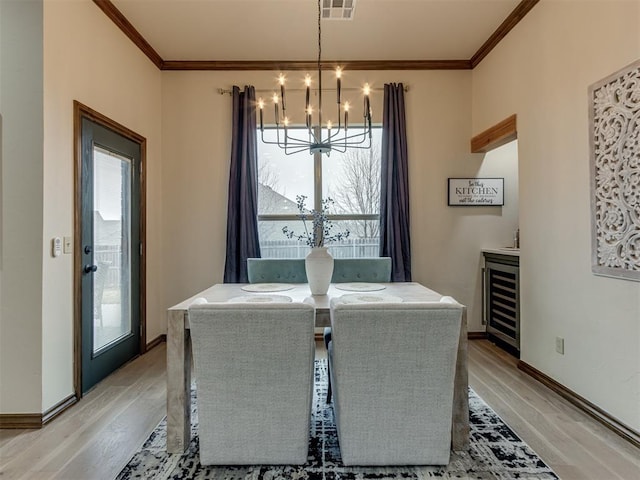 dining room with an inviting chandelier, beverage cooler, crown molding, and light hardwood / wood-style flooring