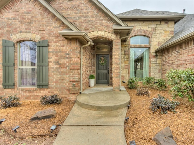 doorway to property with stone siding, brick siding, and roof with shingles