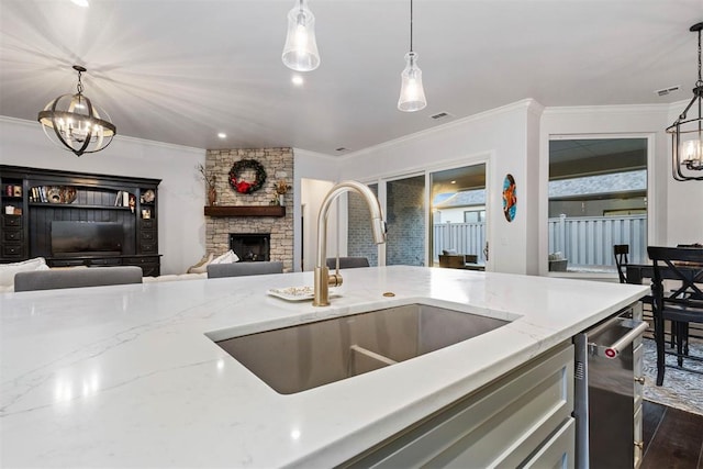 kitchen with a stone fireplace, decorative light fixtures, sink, crown molding, and light stone countertops