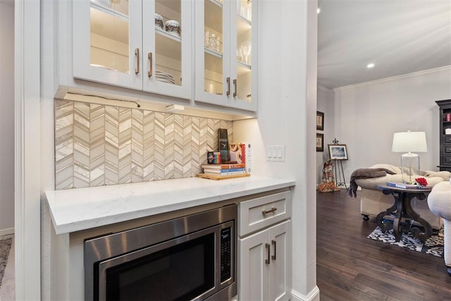 bar with tasteful backsplash, stainless steel microwave, ornamental molding, dark hardwood / wood-style floors, and light stone countertops