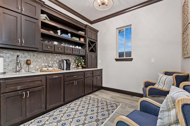 bar with sink, crown molding, dark brown cabinets, and light hardwood / wood-style floors