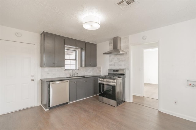 kitchen featuring sink, wall chimney exhaust hood, stainless steel appliances, wood-type flooring, and a textured ceiling