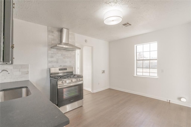 kitchen featuring sink, stainless steel gas range, wall chimney exhaust hood, decorative backsplash, and wood-type flooring