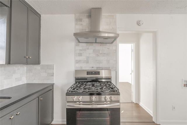 kitchen with gas range, decorative backsplash, gray cabinetry, and wall chimney range hood