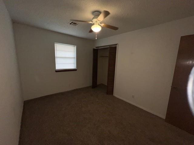 unfurnished bedroom featuring ceiling fan, a closet, a textured ceiling, and dark colored carpet