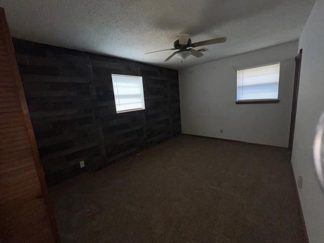 spare room with ceiling fan, wooden walls, and a textured ceiling