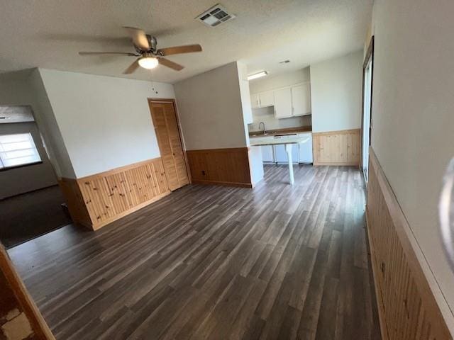 unfurnished living room with wood walls, sink, ceiling fan, a textured ceiling, and dark hardwood / wood-style flooring