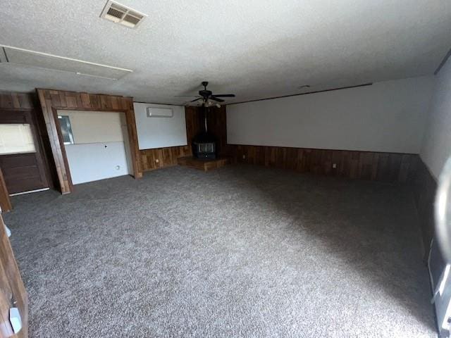 unfurnished living room featuring wood walls, ceiling fan, dark carpet, and a textured ceiling