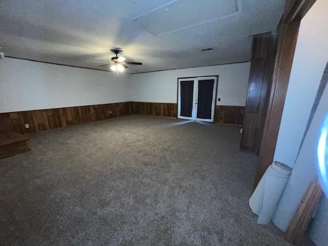 carpeted spare room with ceiling fan, wood walls, and a textured ceiling