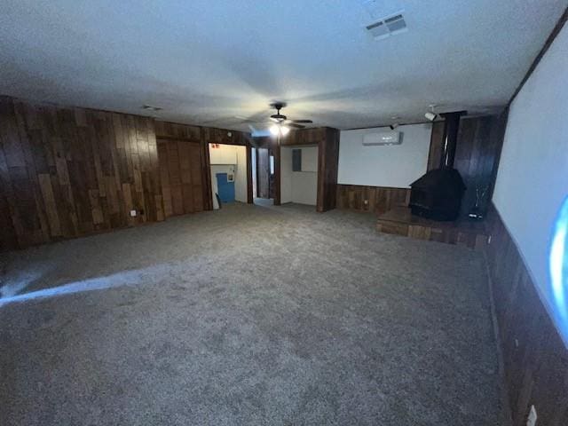 unfurnished living room with carpet floors, a wood stove, ceiling fan, and wood walls