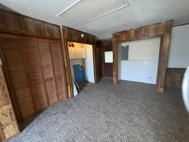 unfurnished bedroom featuring carpet flooring, a textured ceiling, a closet, and wooden walls