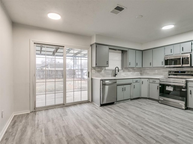 kitchen with tasteful backsplash, gray cabinetry, stainless steel appliances, sink, and light hardwood / wood-style floors