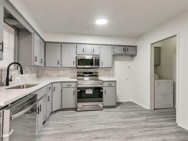 kitchen with appliances with stainless steel finishes, backsplash, light hardwood / wood-style floors, sink, and gray cabinets