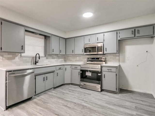 kitchen featuring gray cabinetry, backsplash, sink, light wood-type flooring, and appliances with stainless steel finishes