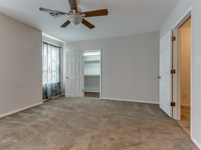 unfurnished bedroom featuring a walk in closet, ceiling fan, a closet, and light carpet