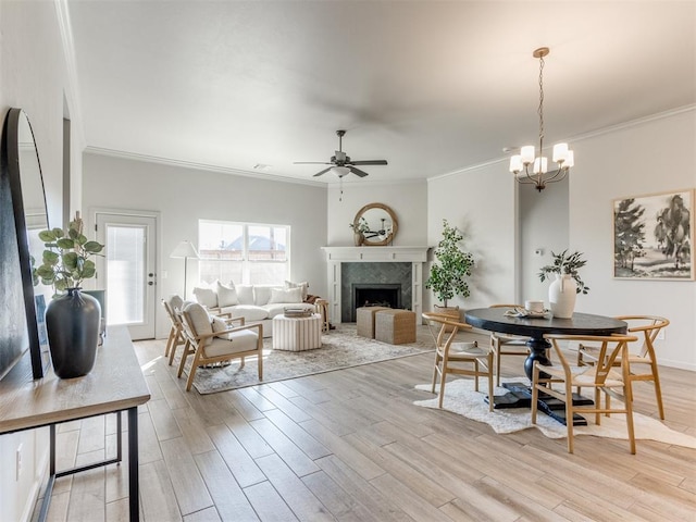 dining area featuring ceiling fan with notable chandelier, ornamental molding, and a fireplace