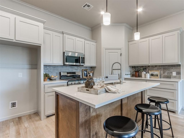 kitchen with sink, hanging light fixtures, decorative backsplash, an island with sink, and stainless steel appliances