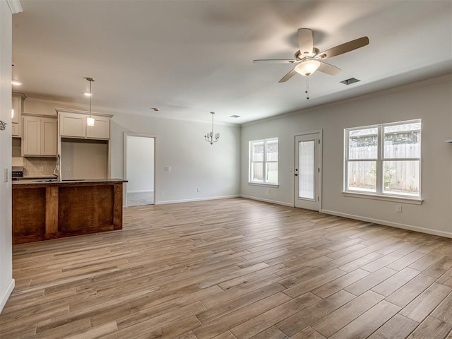 unfurnished living room featuring light wood-type flooring, ceiling fan with notable chandelier, and ornamental molding