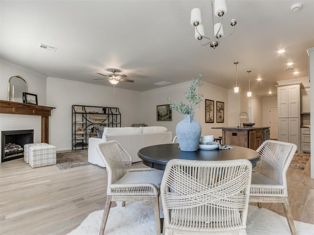 dining area featuring crown molding, a fireplace, visible vents, light wood-type flooring, and ceiling fan with notable chandelier