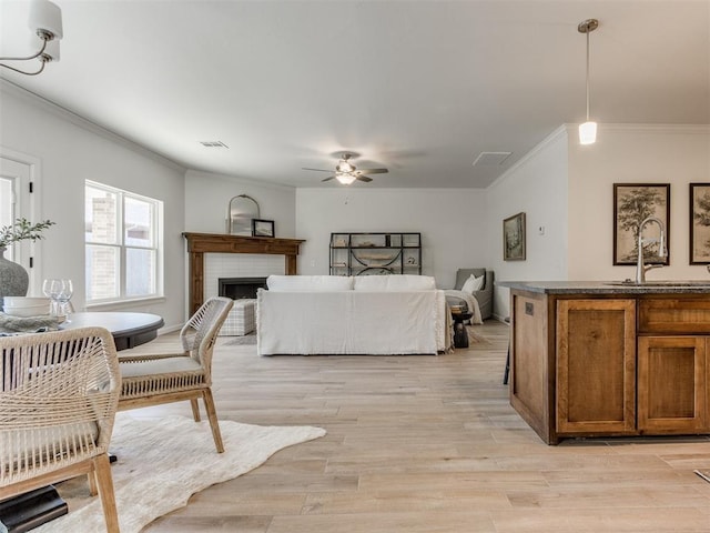 interior space with crown molding, a fireplace, visible vents, a sink, and light wood-type flooring